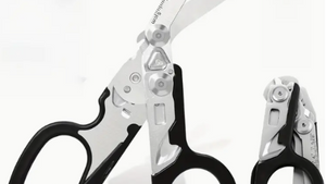 A pair of stainless steel trauma shears with a black handle, displayed alongside its opened case which reveals multiple tools such as a folding knife, ruler, and glass breaker.