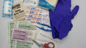 A collection of first aid items including adhesive bandages, sterile gauze, oval eye pad, curlex wrap, gloves, scissor, tweezer, ointment packet, and heavy woven bandages, all displayed on a white surface.